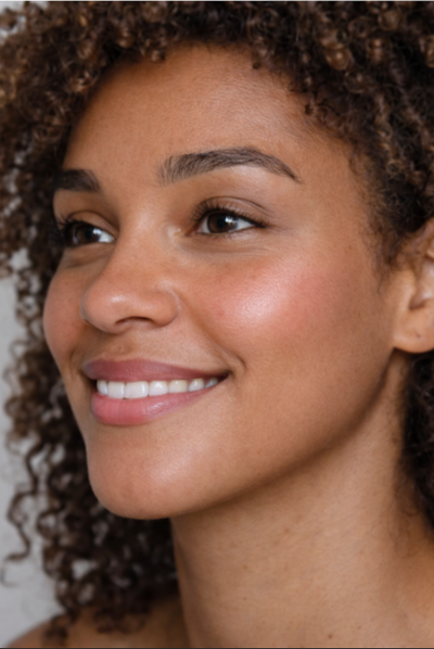 Close-up of a woman with a soft smile and clear face showing her teeth.