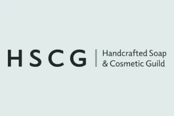 The logo for HSCG (Handcrafted Soap & Cosmetic Guild) in dark gray text on a pale blue-gray background.