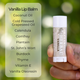 Vanilla lip balm held by a hand with a list of ingredients on a green blurred background.